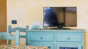 Una habitación con un aparador color turquesa, un televisor encima, una cama con una colcha estampada y una mesita con una caja de pañuelos y el control remoto.