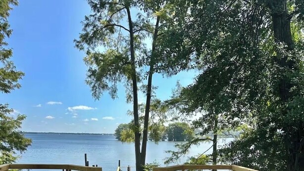 A wooden deck with two Adirondack chairs facing a calm lake, surrounded by trees. - Perfect View of Cross Lake (Shreveport)