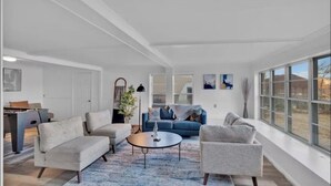 A spacious living room with a blue sofa, two armchairs, a coffee table, and a large window offering a view of the outdoors. - Perfect View of Cross Lake (Shreveport)