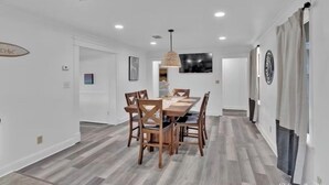 A dining area with a wooden table and chairs, a hanging light fixture, and a wall-mounted TV. - Perfect View of Cross Lake (Shreveport)