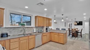 A modern kitchen with wooden cabinets, a large island, and a dining area with a table and chairs. - Perfect View of Cross Lake (Shreveport)