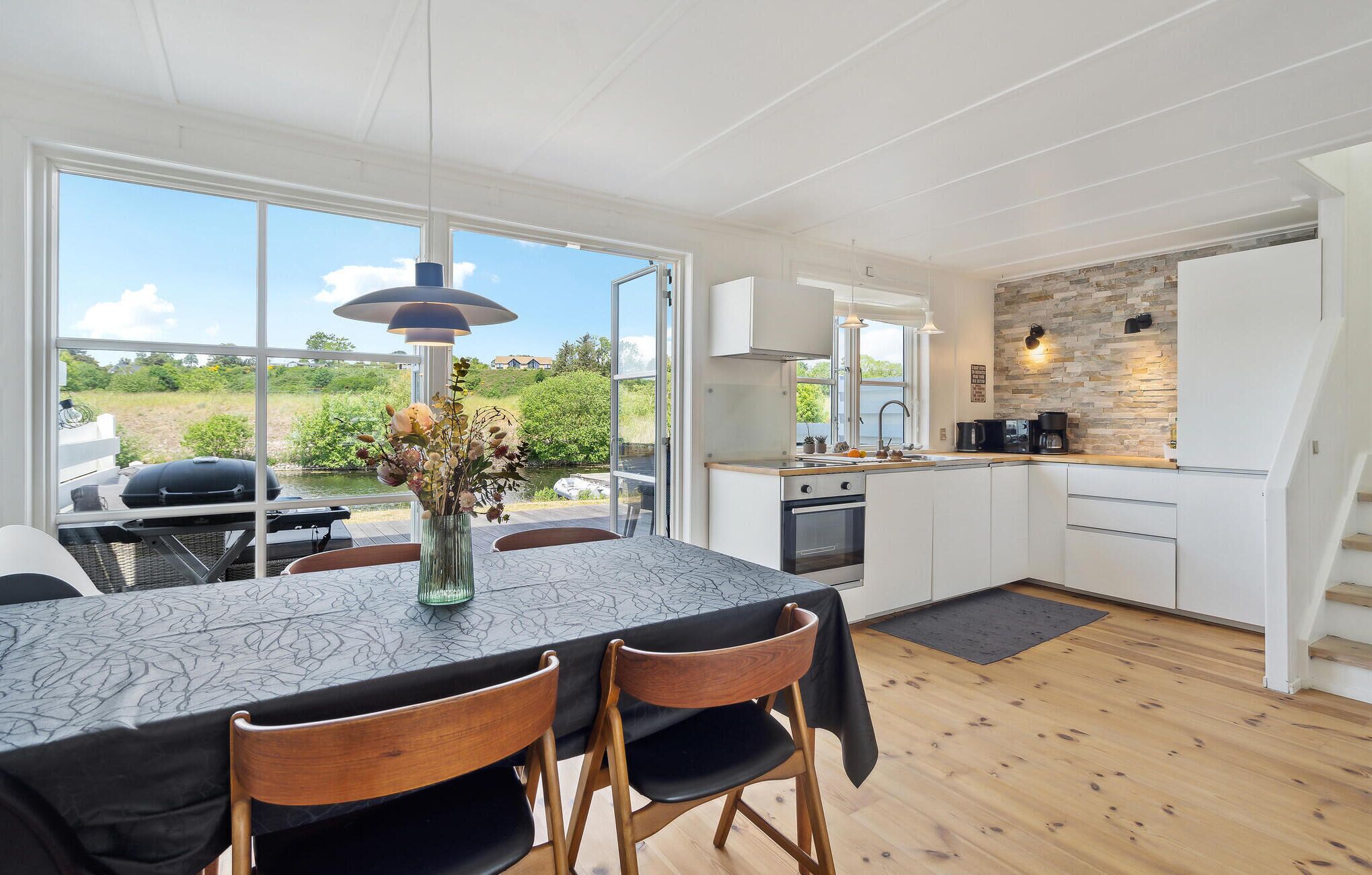 A modern kitchen with white cabinets, a stone backsplash, and a dining area with a table and chairs.
