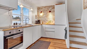 Uma cozinha moderna com armários brancos, forno embutido, janela ampla e painel de pedra.