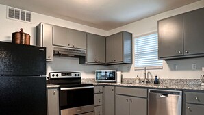 A modern kitchen with stainless steel appliances, grey cabinets, and a wooden floor. - No Minimum Stay! No Chores! Kids allowed (Port O'Connor)