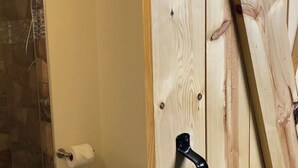 A bathroom with a toilet, a shower area, and a wooden door with a black handle.