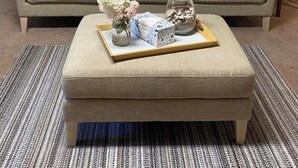 A living room with a beige sofa, two matching pillows, a small side table, a tray with decorative items, and a wall-mounted shelf with a plate and small objects.