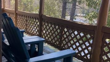 Um deck de madeira com cadeiras Adirondack e um guarda-corpo treliçado.