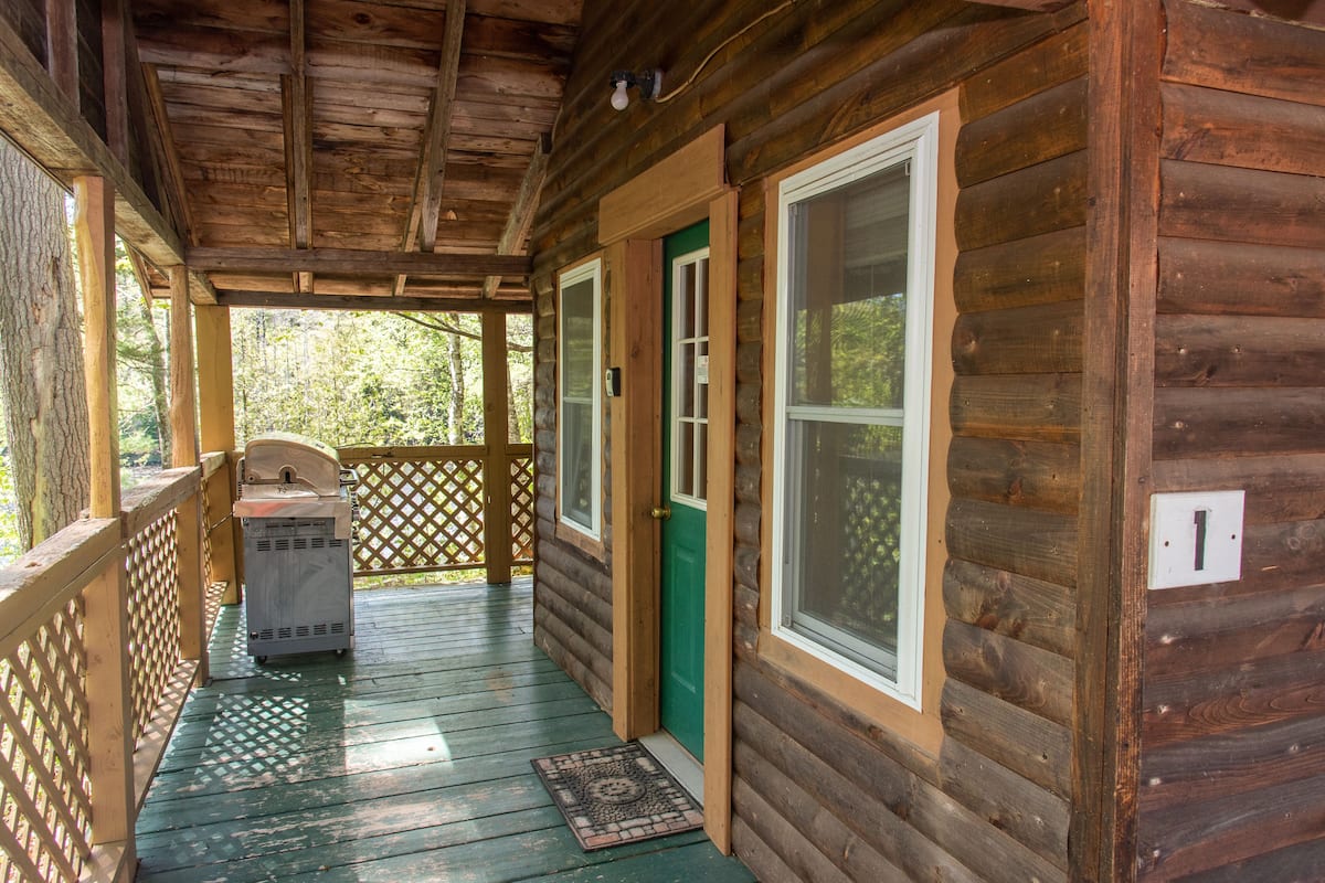 A wooden cabin with a porch, a green door, and a window.
