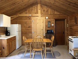 A cabin-style kitchen with wooden walls, a dining table with four chairs, a refrigerator, a microwave, and a stove.
