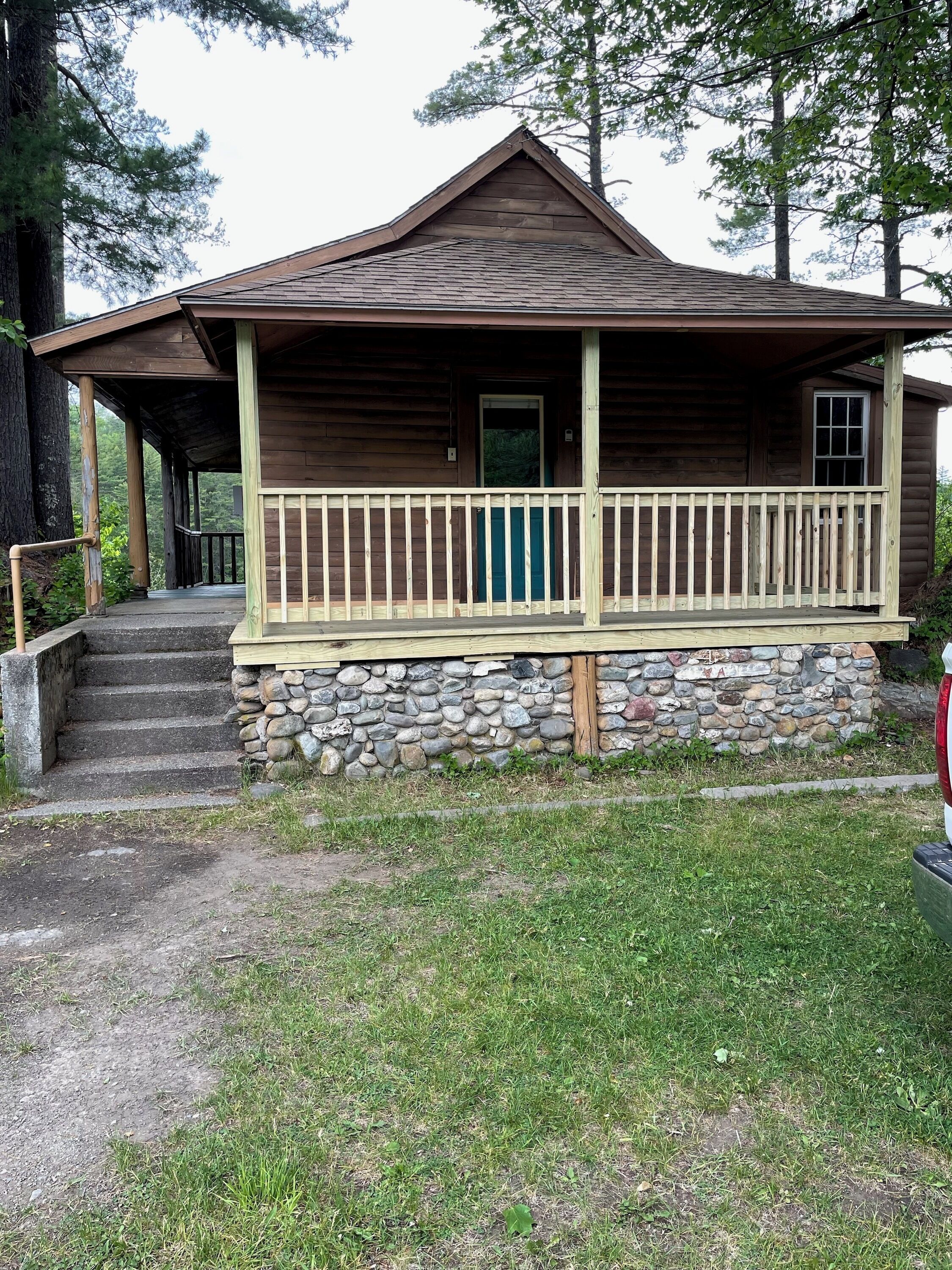 Une cabane en bois avec des fondations en pierre, une véranda dotée d’une balustrade et une porte.