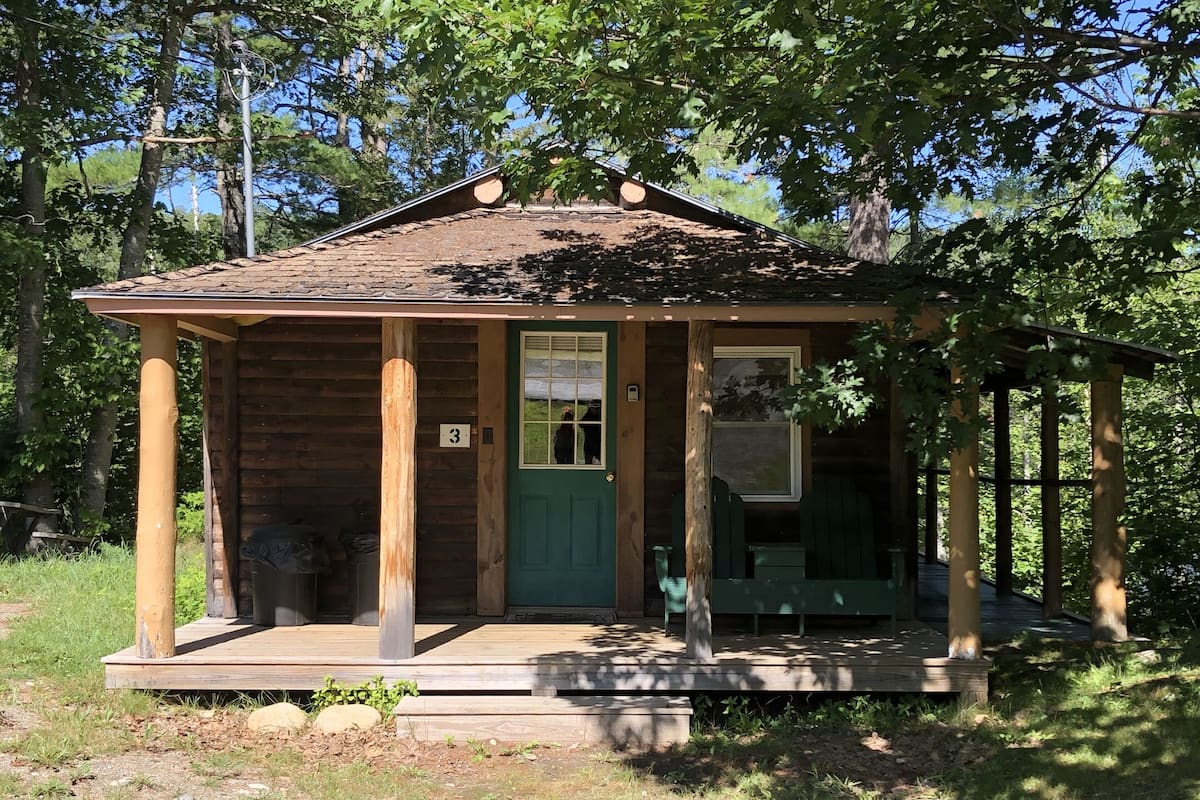 A rustic wooden cabin with a green door, a porch, and a small window.