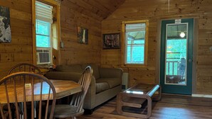 Interior acogedor de una cabaña con una mesa de madera, sillas, un sofá y un pequeño banco.