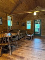 A cozy cabin interior with a wooden dining table, chairs, a sofa, and a small bench.