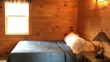 A wooden cabin room with a bed, a nightstand, and a window.