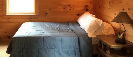 Een houten kamer met een bed, een nachtkastje en een raam.
