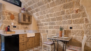 Une cuisine rustique avec un mur en pierre, des armoires en bois, un lave-vaisselle noir et une table avec des chaises.