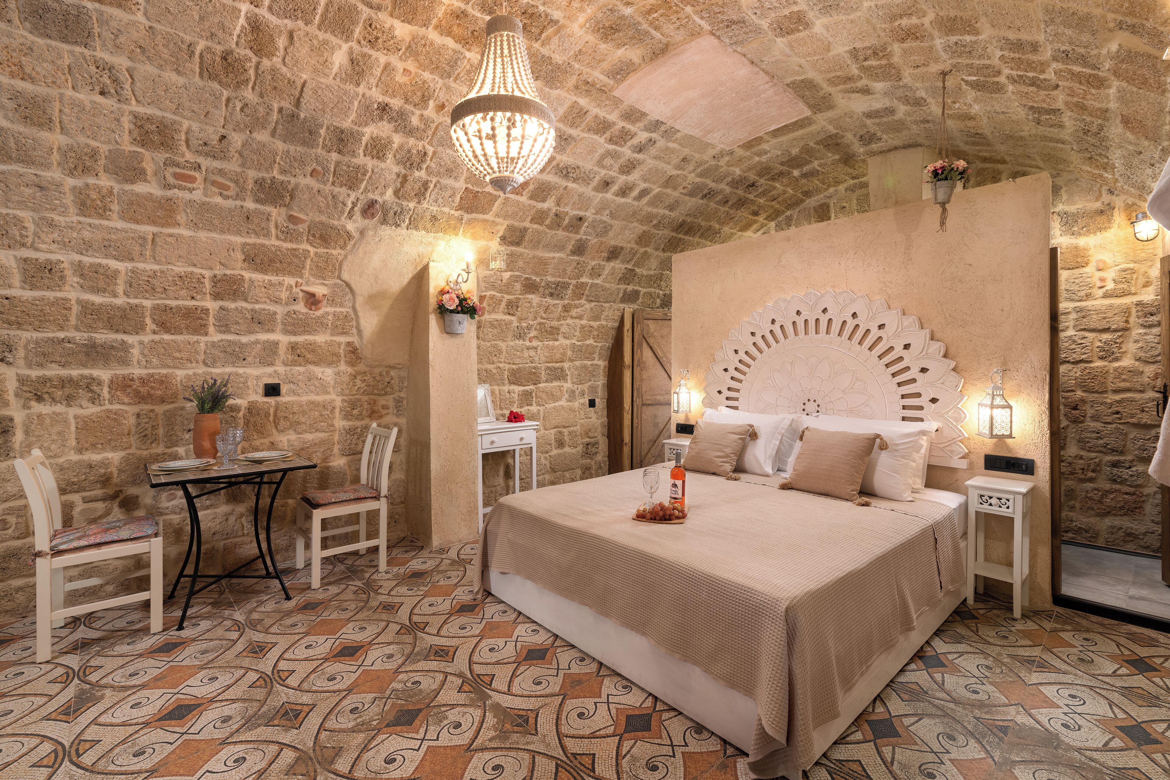 Camera da letto con parete in pietra, un letto con testiera decorativa, un tavolino con sedie e un lampadario.