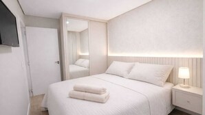 A bedroom with a bed, a nightstand, a lamp, a mirror, and a door. - Top apartment, 4 minutes from the covered street by car, kids' area, heated pool, gym. (Gramado)