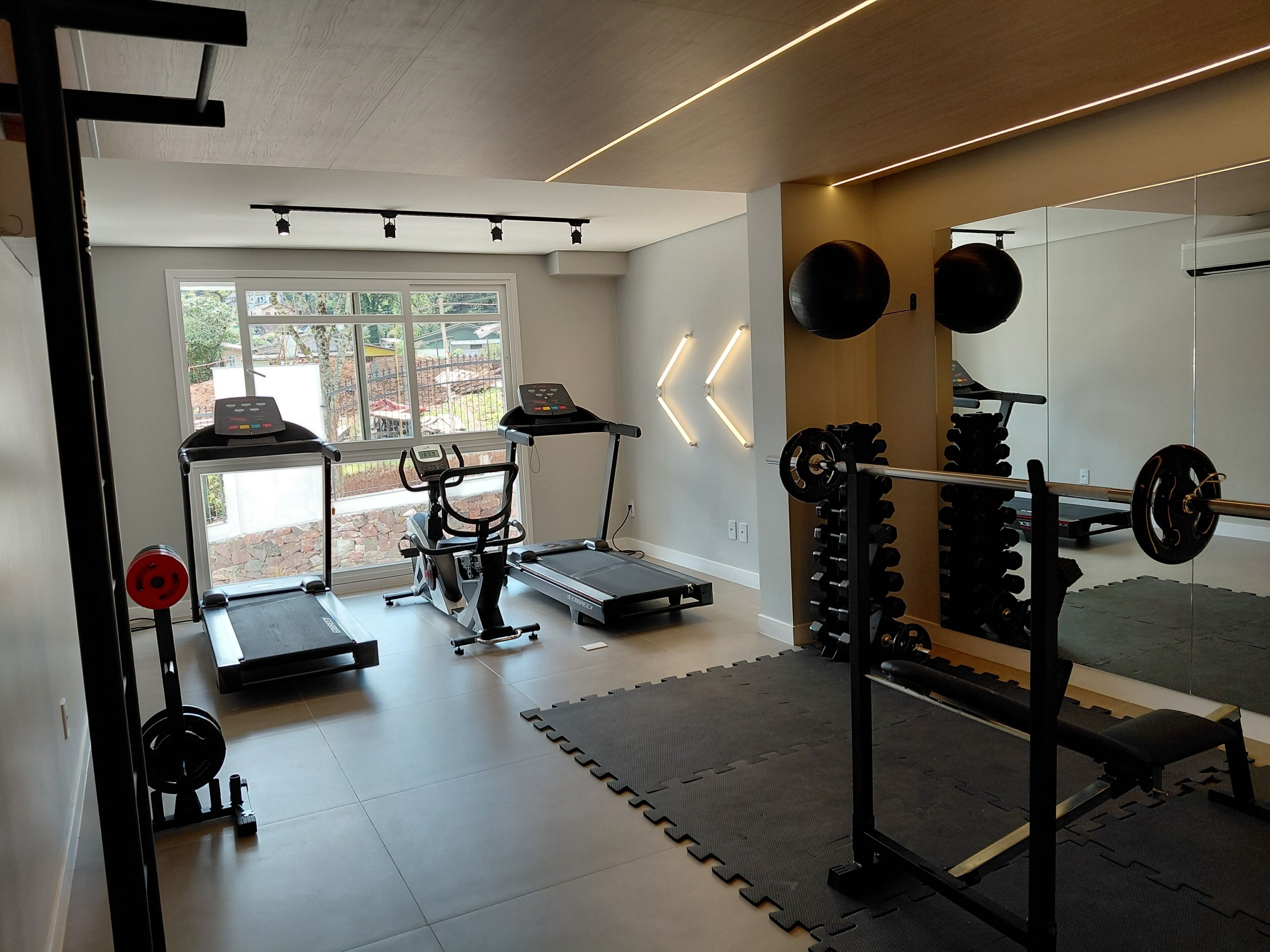 Une salle de sport à domicile équipée de matériel d’exercice, notamment un tapis de course, un vélo d’appartement et un appareil de musculation.