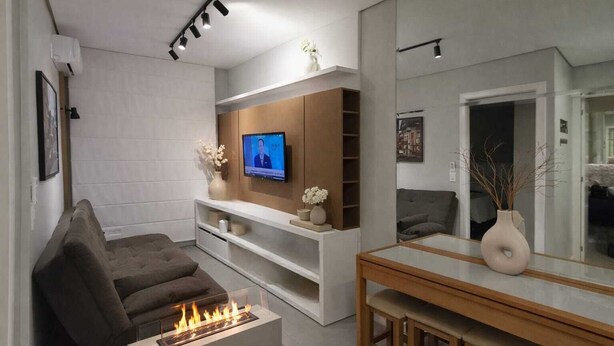 A modern living room with a flat-screen TV, a fireplace, a sofa, and a dining area with a mirror. - Top apartment, 4 minutes from the covered street by car, kids' area, heated pool, gym. (Gramado)