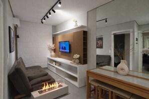 Una sala moderna con televisor de pantalla plana, chimenea, sofá y comedor con espejo.