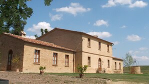 A two-story building with a tiled roof, multiple windows, and a small patio area with outdoor furniture. - Aria Apartment: Romantic Stay with Breakfast (loc Resta Buonconvento)