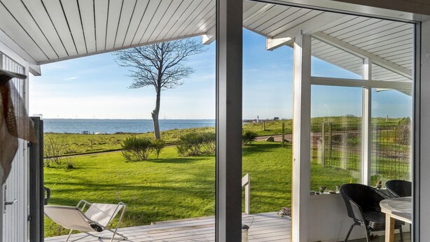 A modern outdoor patio with a glass door leading to a grassy area with a view of the sea and a lighthouse.