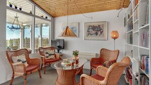 A spacious living room with wicker furniture, a glass coffee table, and a bookshelf filled with books.