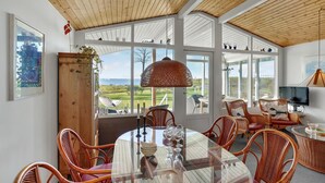 A spacious dining area with a large round table, wicker chairs, and a view of the sea through large windows.