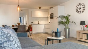 A modern apartment with a living area, kitchen, and dining space. It includes a sofa, a dining table with chairs, a potted plant, and a clock on the wall. - Amazing apartment in Oostende with WiFi (Oostende)