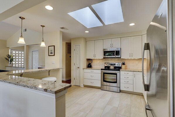 A modern kitchen with a central island, stainless steel appliances, and a skylight.