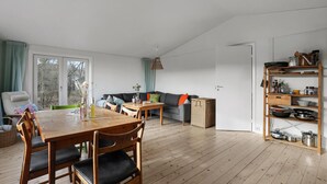 A spacious living area with a wooden dining table, a sofa, and a kitchen area with shelves. - Cozy home in Nexø with house sea view (Nexø)