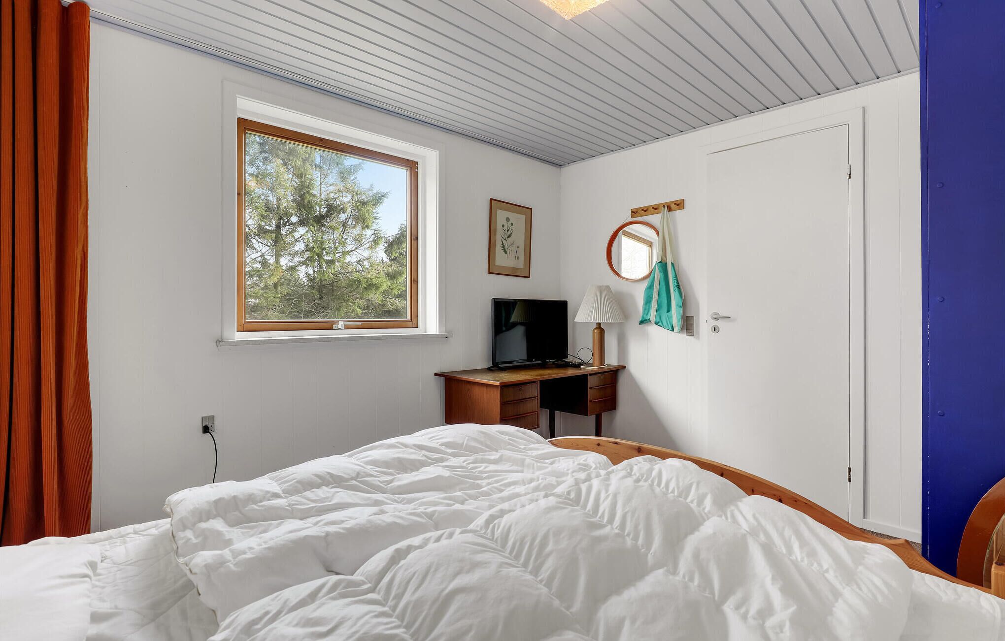 Ein Schlafzimmer mit Bett, Schreibtisch, Fernseher und Fenster mit Blick auf Bäume.