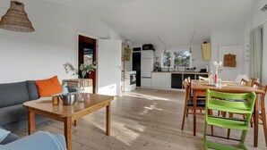 A modern kitchen with white cabinets, a built-in oven, and a microwave. There is a dining area with a wooden table and chairs, and a living room with a sofa and a coffee table. - Cozy home in Nexø with house sea view (Nexø)