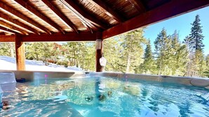 Una vasca idromassaggio sotto un gazebo in legno, con un paesaggio innevato e alberi sullo sfondo.