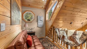 Un accogliente interno di una baita con soffitto in legno, un divano in pelle, una coperta fantasia e una rustica ringhiera in legno.