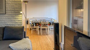 Ein gemütliches Zimmer mit Holzboden, einer Couch, einem Tisch mit Stühlen und einem Fernseher.