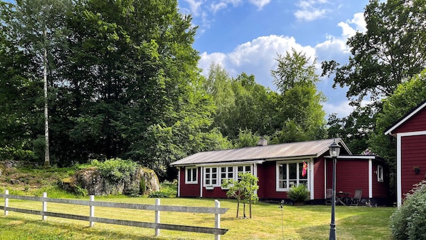 Ein rotes Holzhaus mit Veranda, umgeben von einem Holzzaun und üppigem Grün.