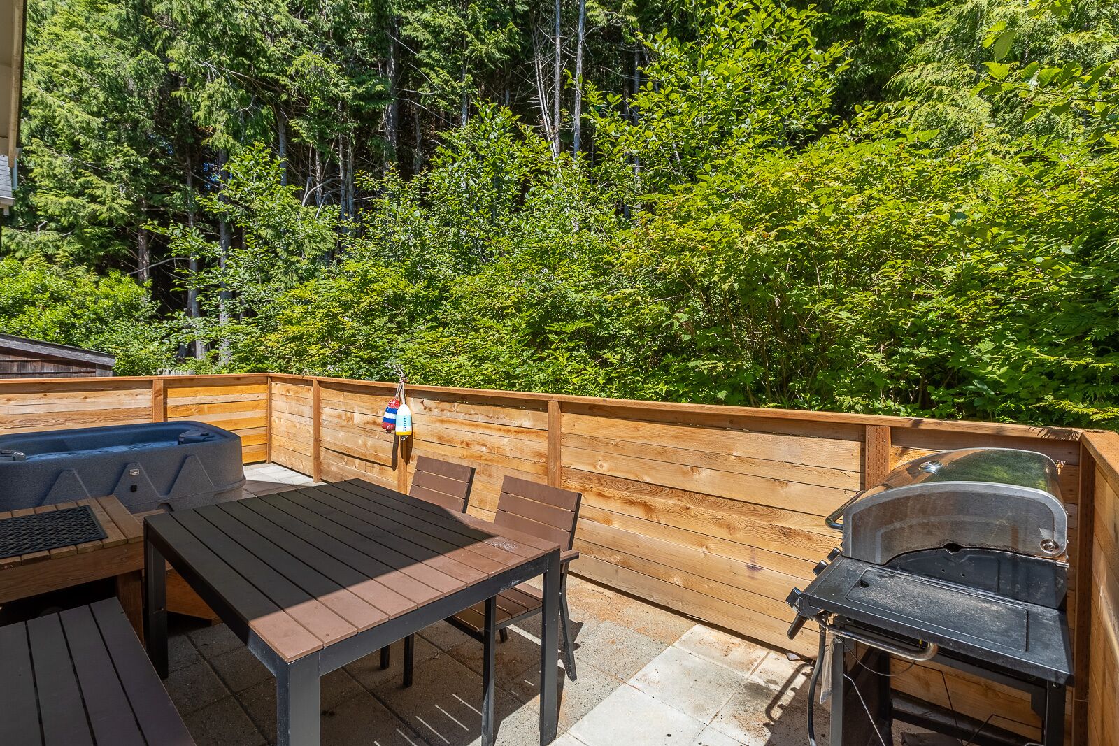 A wooden deck with a hot tub, table, chairs, and a grill.