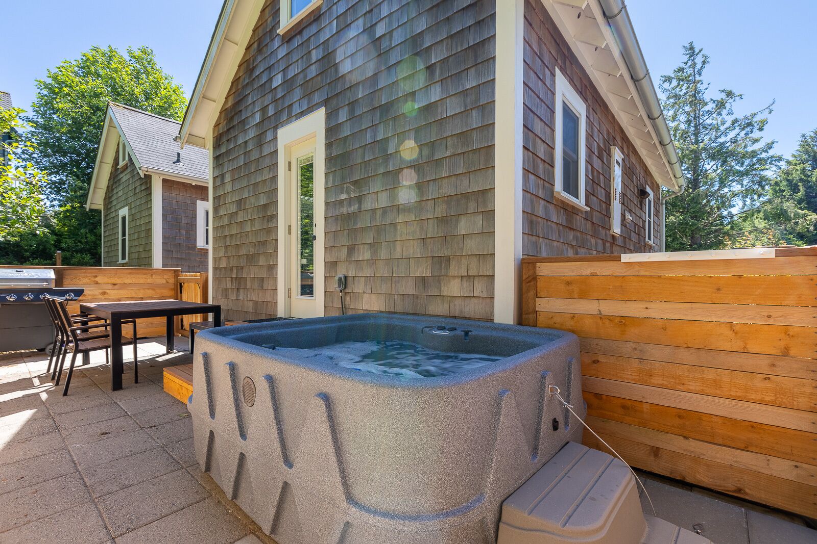 Un jacuzzi en un patio trasero con terraza de madera, una parrilla y una mesa con sillas.