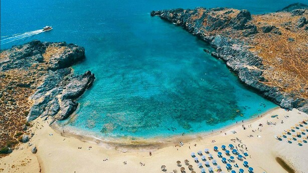 An aerial view of a beach with clear turquoise waters, rocky outcrops, and a sandy shore with beach umbrellas and sun loungers. - Villa 7 Seas - With Amazing View (Lefkogia)