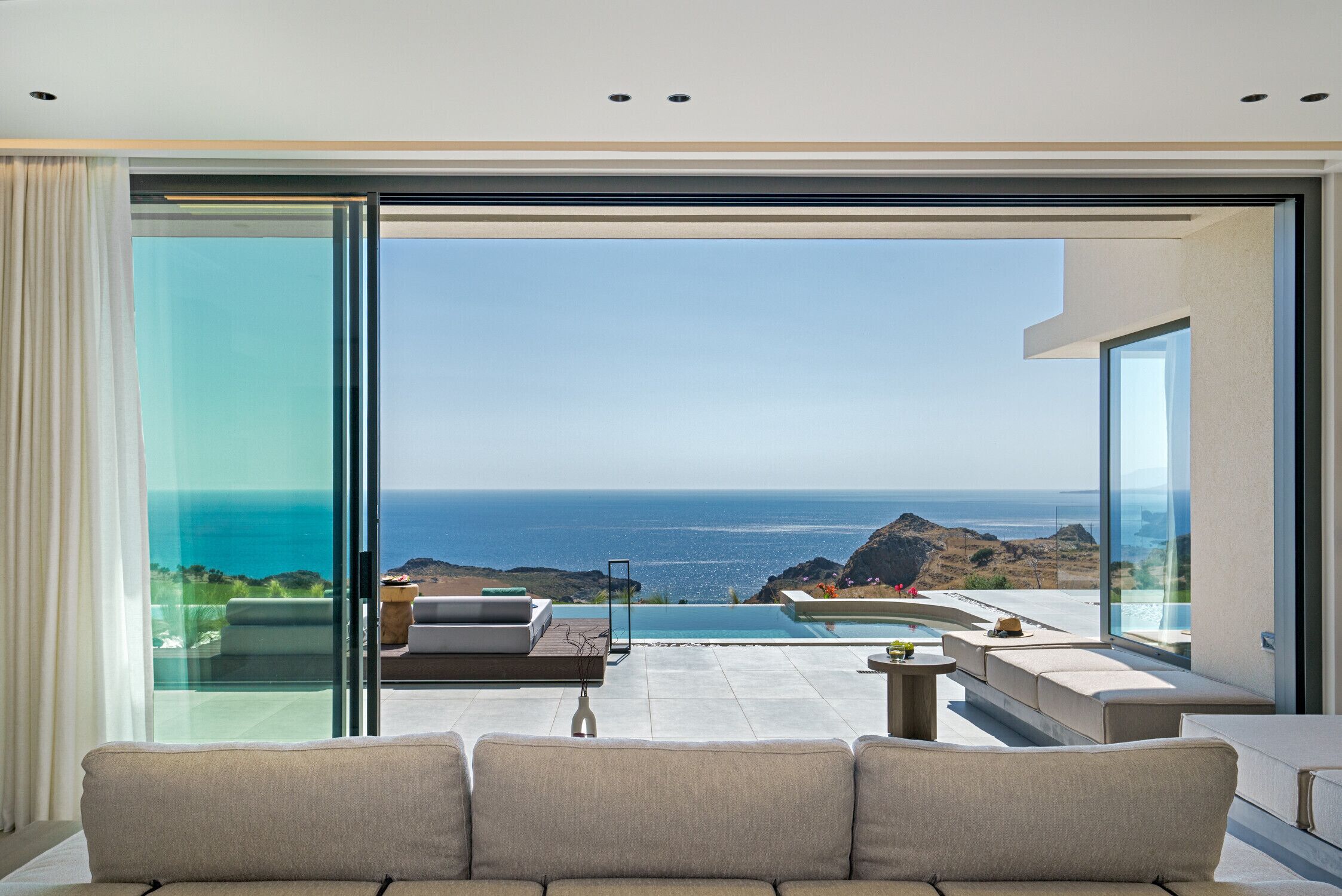 A modern living room with a large glass door leading to a balcony with a view of the ocean.