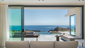 A modern living room with a large glass door leading to a balcony with a view of the ocean. - Villa 7 Seas - With Amazing View (Lefkogia)