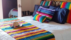 A bed with a colorful striped blanket and pillows, a wooden headboard, and a window with a view of the outdoors.