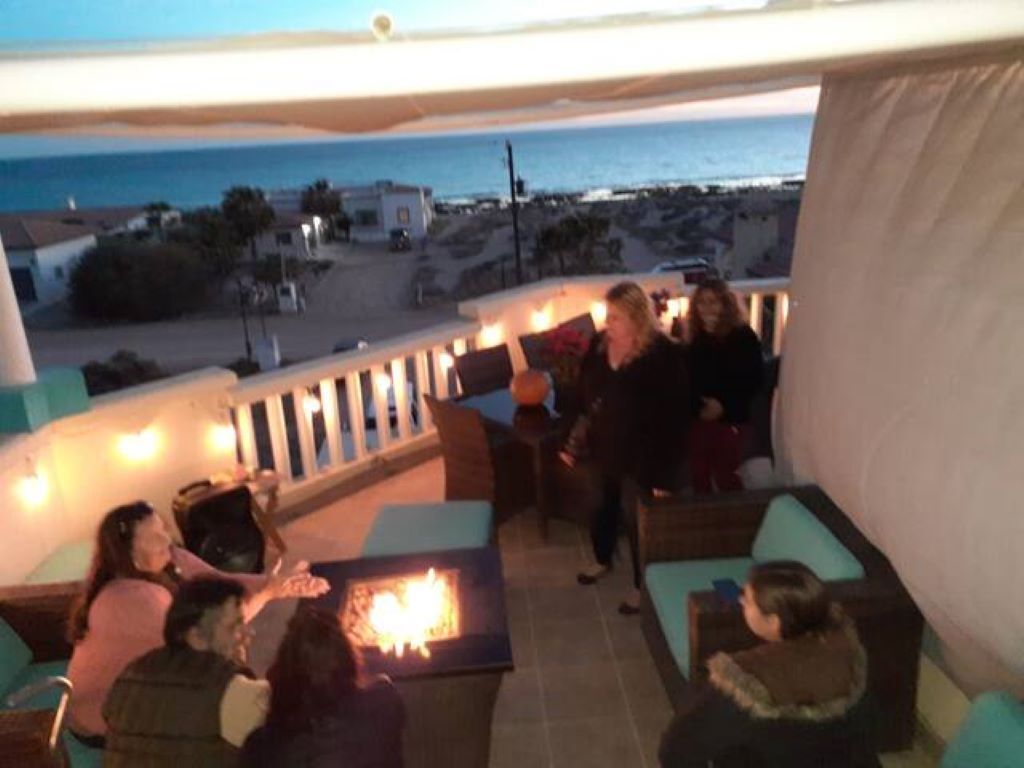 A terrace with outdoor seating and a fire feature, overlooking a beach and ocean.