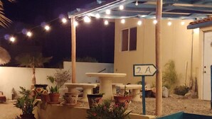 An outdoor patio area with potted plants, a table, and chairs under string lights.