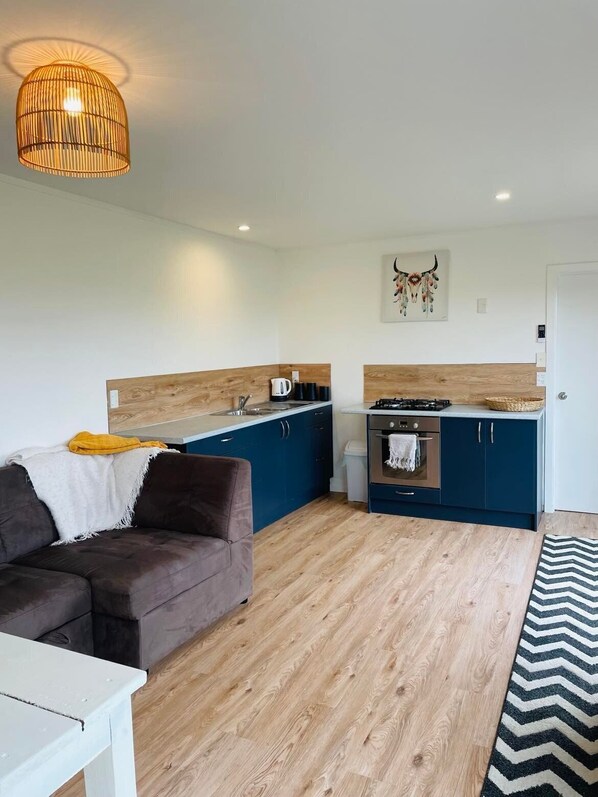 A compact living space with a kitchenette, a sofa, a dining table, and a hanging light fixture.