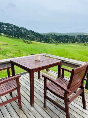 A wooden deck with a table and chairs overlooking a grassy field and forest.