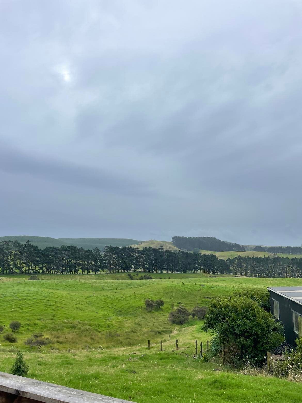 A rural landscape with a green field, a fence, and a building in the foreground.