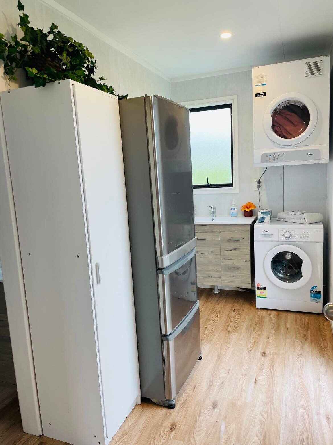 A compact kitchen with a stainless steel refrigerator, a double oven, a washing machine, and a window with a view.